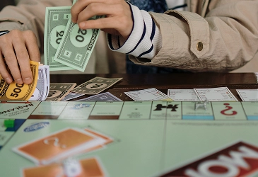 Ręce graczy liczą kolorowe banknoty z gry planszowej na stole